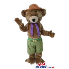 Brown bear wearing a brown hat, green trousers and a purple