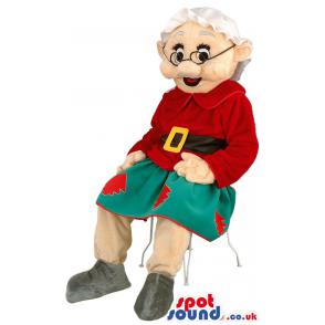 Grandmother mascot is sitting in a chair red and green clothes