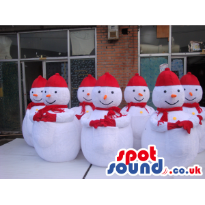 Seven Snowmen Mascots Wearing A Red Scarf, Gloves And Hat -