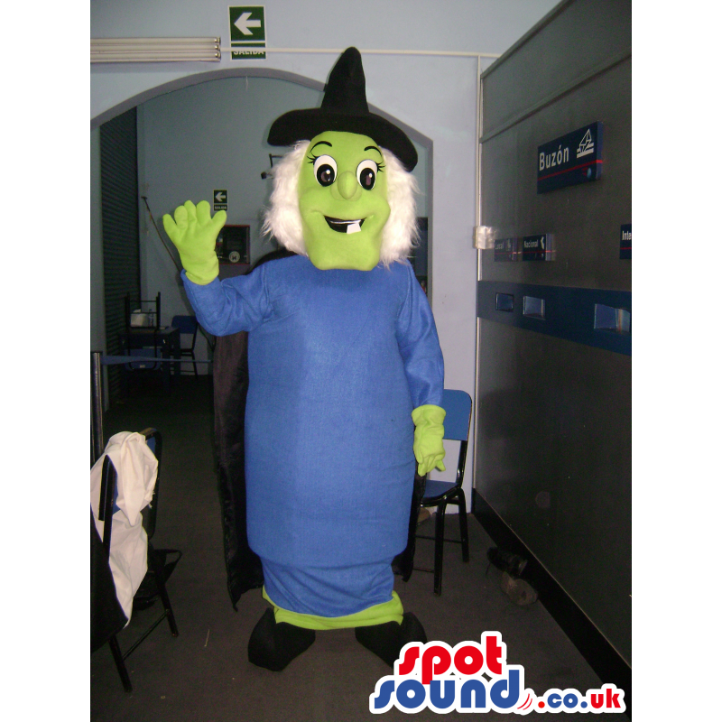 Green witch mascot with blue dress, black pointy hat and cape -