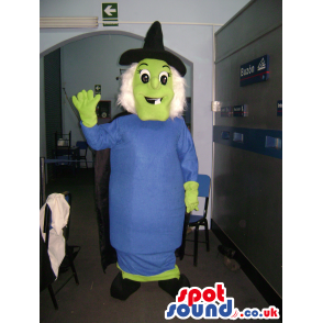 Green witch mascot with blue dress, black pointy hat and cape -